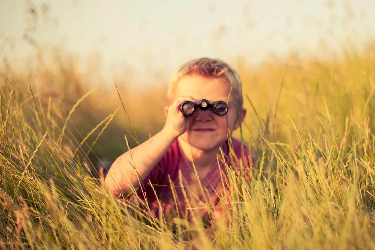 boy in grass field with binoculars search